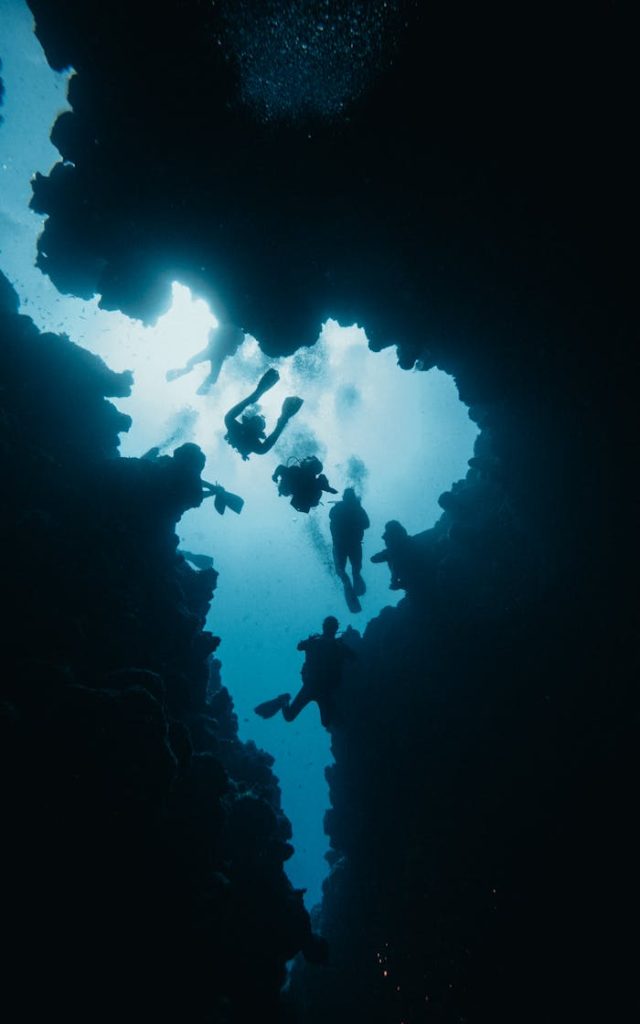 Koh Tao Diving Silhouetted scuba divers explore a dramatic underwater cave.